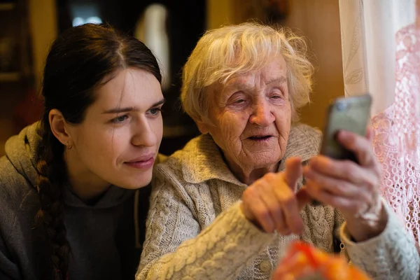Yaşlı Bir Bayan Yetişkin Torunu Ile Bir Akıllı Telefona Bakıyor — Stok fotoğraf