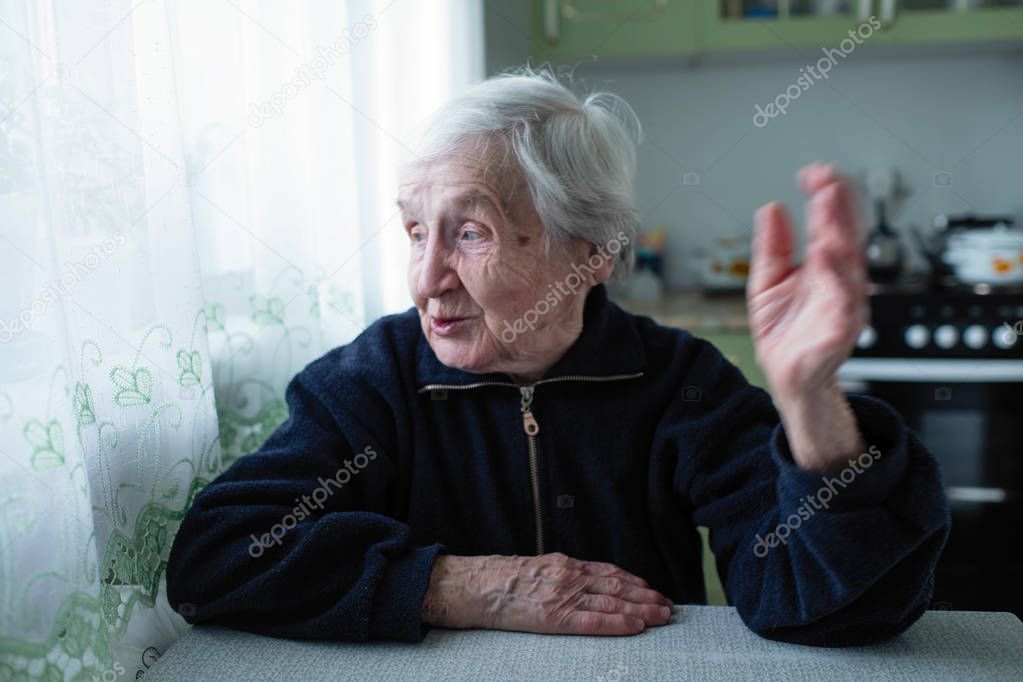 The old woman speaks expressively sitting at the table.