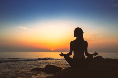 Akşam okyanus kıyısında Lotus pozisyonda kadın yoga silueti.