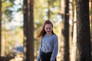 Twelve-year-old girl with long red hair posing in a summer pine Park.