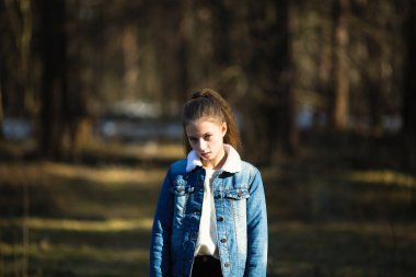 Twelve-year-old girl in a denim jacket posing in a summer pine Park.
