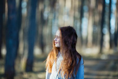 Twelve-year-old cute girl with long red hair posing for the camera in the park, photo shoot outdoors.