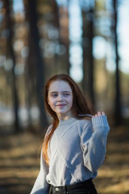 Twelve-year-old cute girl with long red hair posing for the camera in the park, photo shoot outdoors.