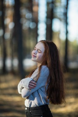 Twelve-year-old cute girl with long red hair posing for the camera in the park, photo shoot outdoors.