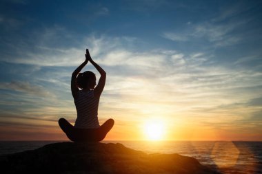 Siluet genç kadın gevşeme Lotus gün batımında plajda poz yoga pratik.