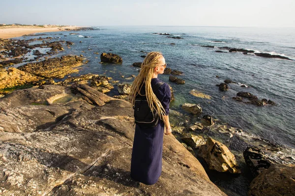 一个年轻女子长光恐怖锁站在岩石岸边的海洋看冲浪 — 图库照片