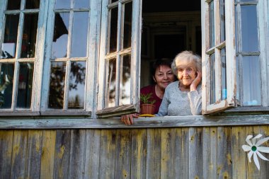 Yaşlı kadın ve onun yetişkin kızı köy evinin penceresinden dışarı bakıyor.