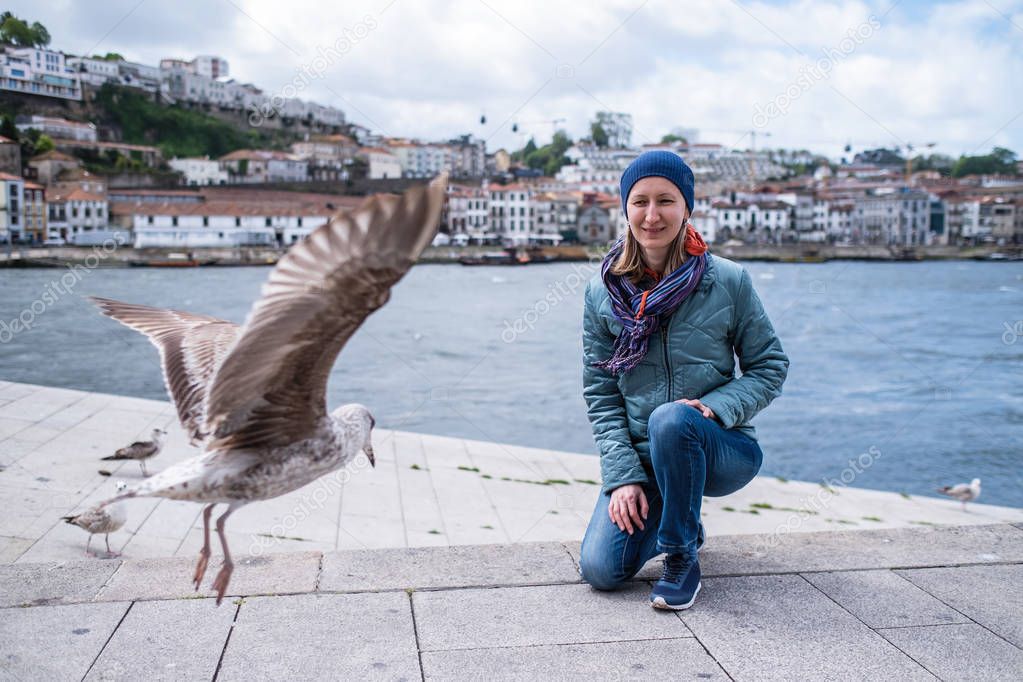 Young woman among seagulls on embankment in Ribeira of Douro river, Porto, Portugal.