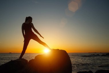 Muhteşem gün batımında plajda fitness egzersizleri yapan genç kadının silueti. Yoga ve sağlık.