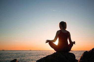 Yumuşak sıcak gün batımı sırasında okyanus kıyısında Yoga kadının silüeti.
