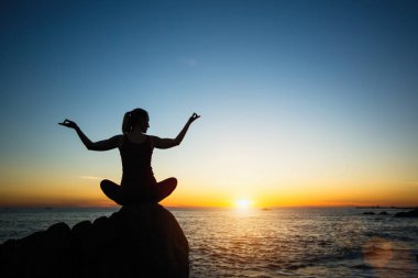 Siluet genç kadın keyifli günbatımı plajda yoga pratik.