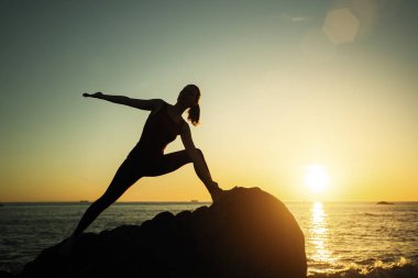 Yoga silueti genç kadın gün batımında sahilde spor yapıyor.