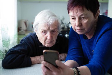 Yetişkin bir kadın yaşlı bir kadına akıllı telefon ekranını gösterir.