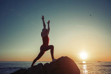 Gün batımında deniz kıyısında egzersiz yapan yoga kadının silueti.