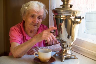An old woman drinks tea from a Russian samovar. clipart