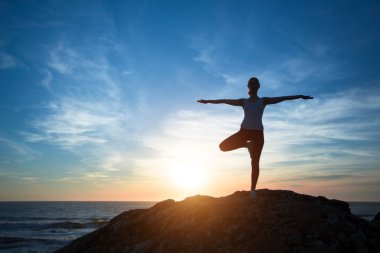 Siluet genç kadın gün batımında plajda yoga yapıyor.