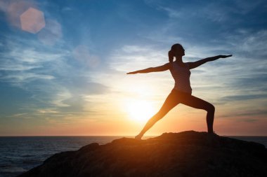 Siluet genç kadın gün batımında plajda yoga yapıyor. Huzur ve konsantrasyon.