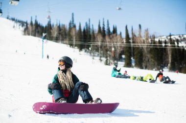 Karlı yamaçta oturan kadın snowboardcu..