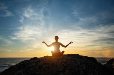 Siluet genç kadın gün batımında plajda yoga yapıyor. Huzur ve konsantrasyon.