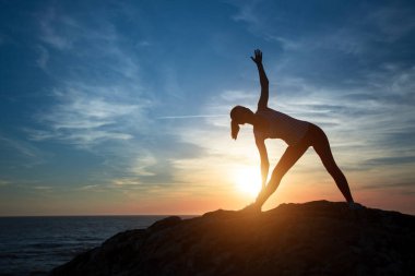 Kadın yoga silueti, deniz kıyısında gün batımı sırasında konsantrasyon egzersizleri gerçekleştirir.