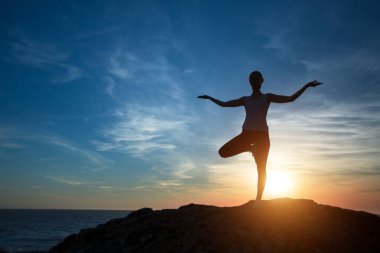 Kadın yoga silueti, deniz kıyısında gün batımı sırasında konsantrasyon egzersizleri gerçekleştirir.