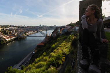 Douro nehri üzerinde Dom Luis I köprü karşısında oturan genç kadın, Porto, Portekiz.