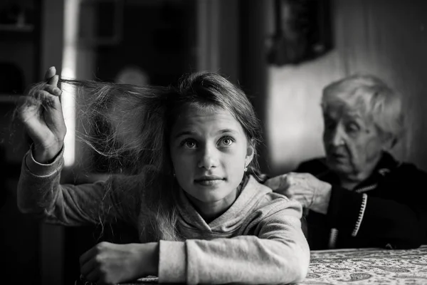 Granny, old woman braids her great-granddaughter\'s hair. Black and white photography.
