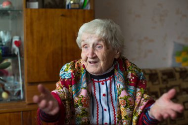 Parlak giysiler ve masada oturan bir eşarp jestleri yaşlı bir kadın.