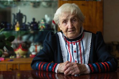 Masada oturan parlak giysiler içinde yaşlı kadın.