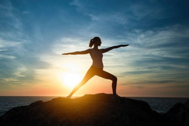 Yoga kadın Assane Warrior pozisyonunda meditasyon. Güzel bir gün batımı sırasında deniz kıyısında siluet.
