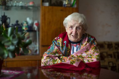Masada oturan parlak kıyafetlerle yaşlı kadının portresi.