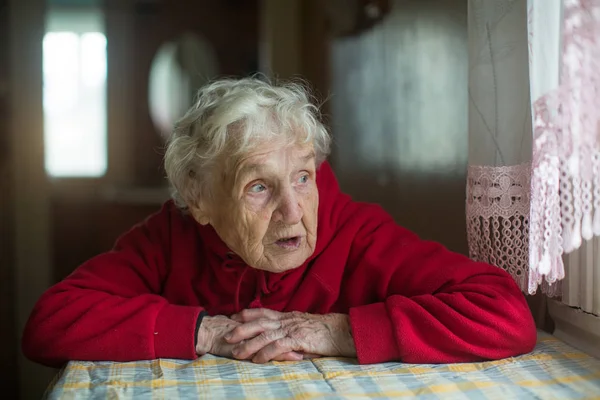 Kırmızı Ceketli Gri Saçlı Yaşlı Kadın Pencereden Dışarı Bakıyor — Stok fotoğraf