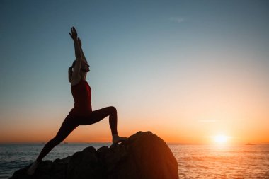 Muhteşem gerçeküstü gün batımı sırasında deniz plajında yoga yapan kadının silueti. 