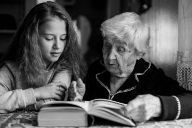 Küçük sevimli kız, yaşlı büyük büyükannesi kitap okuyor. Siyah beyaz fotoğraf.