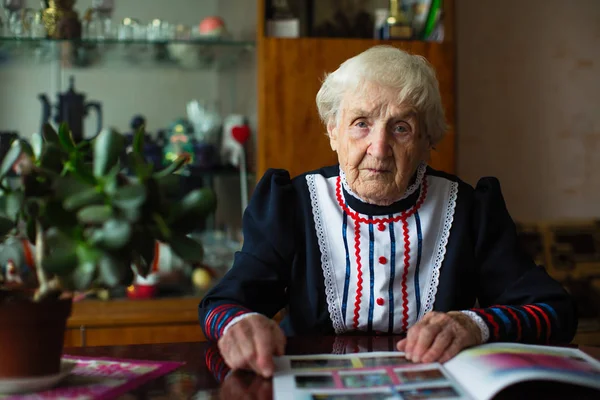 Strict elderly woman in Slavic clothes sitting reading a magazine.