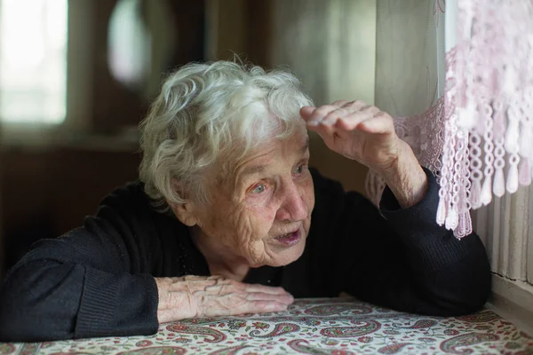 Yaşlı kadın evinin penceresinden dışarı bakar.