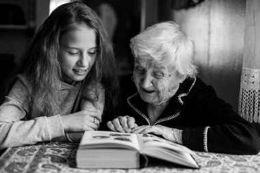 Yaşlı kadın sevgili torununa kitap okuyor. Siyah beyaz fotoğraf.