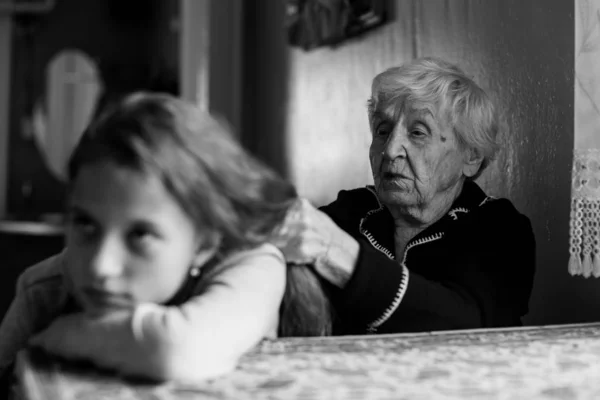 Granny braids her great-granddaughter\'s hair. Black and white photo.