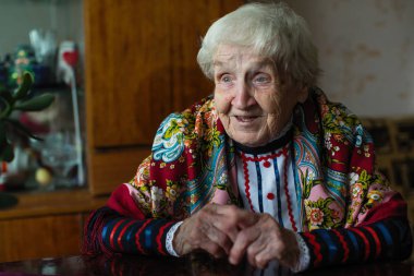 Masada oturan parlak etnik giysiler içinde yaşlı gri saçlı kadın.