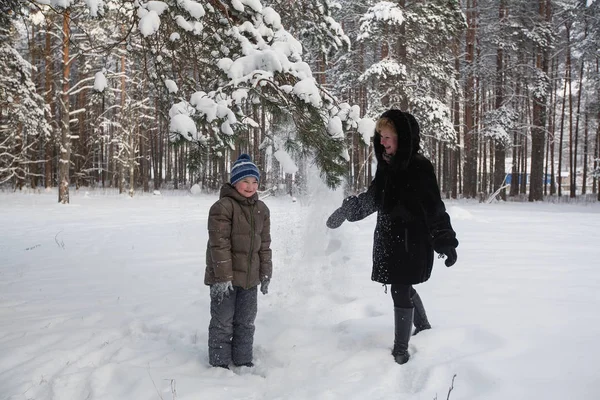 雪の冬の森で小さな息子と遊ぶ若い女性 — ストック写真