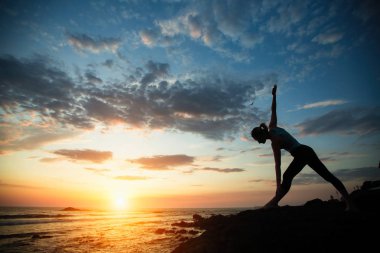 Genç kadın şafak vakti deniz kıyısında egzersiz yapıyor. Yoga silueti. 