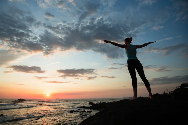 年轻的健身女性在海岸练习瑜伽在一个惊人的日落 — 图库照片