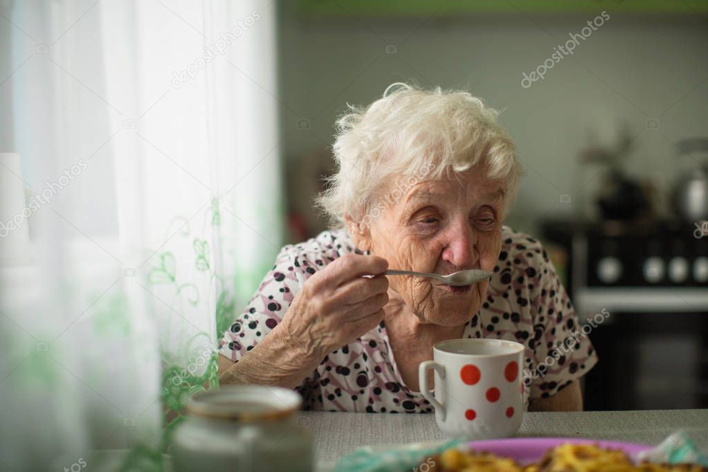 Old woman frandma is sitting in the kitchen drinking tea. 