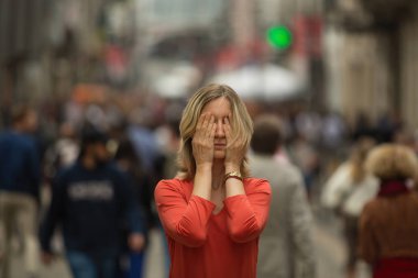 Genç depresif kadın kalabalık bir caddenin ortasında duran elleriyle gözlerini kapatır. 
