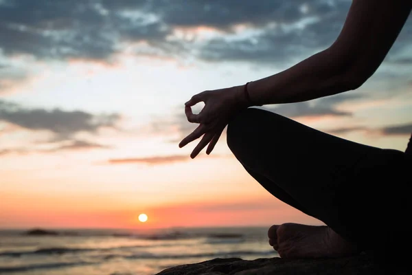 Silhouette of yoga woman close-up meditation on the sea during sunset.