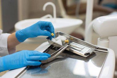 Hands female dentist holding dental tools and teeth over medical office background. Medicine and stomatology concept.