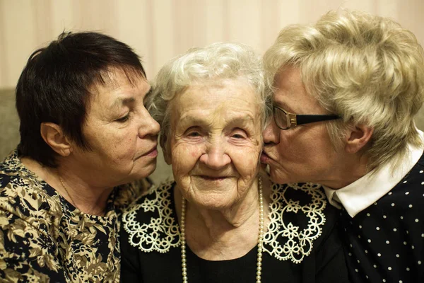 An old woman with two adult daughters sitting and hugging on a sofa.