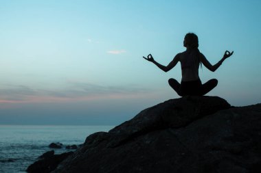 Siluet genç kadın gerçeküstü batımında sahilde Yoga uygulamak.