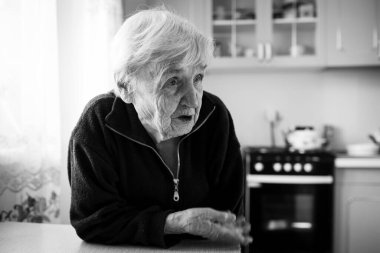 An old woman in the kitchen by the window in his house. Black and white photo.