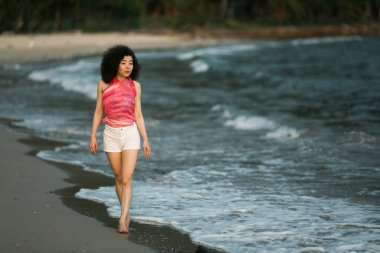Mixed race woman walks along the edge of the surf on the sea beach.